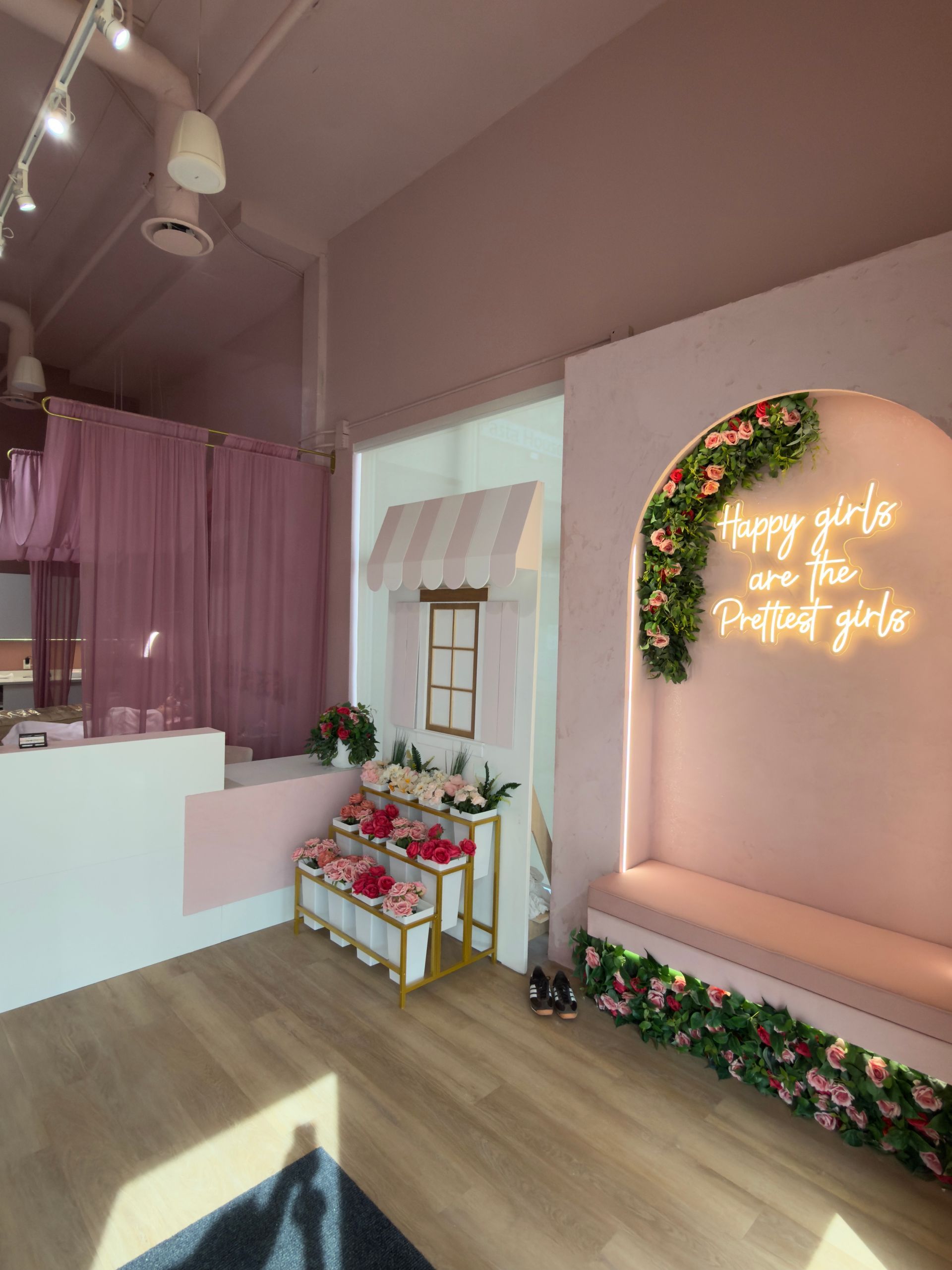 Pink boutique interior with floral decor, glowing neon sign, and a white reception counter