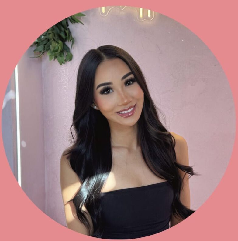 Smiling woman in a black strapless top against a pink wall with hanging greenery