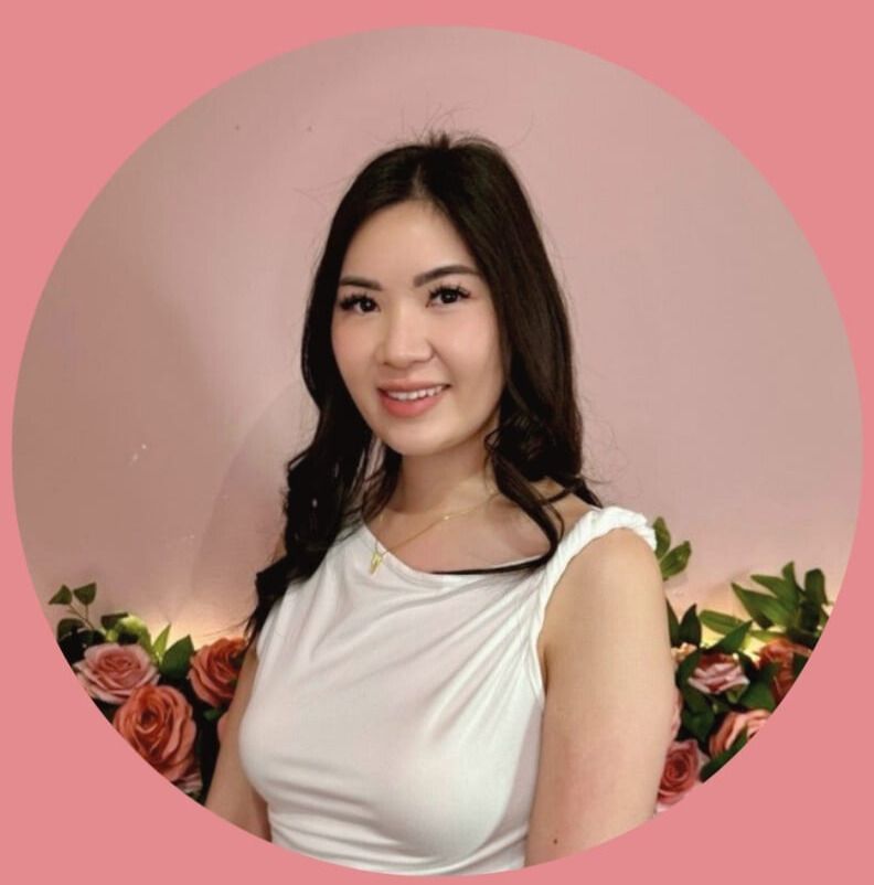 Woman in a white dress smiling against a pink backdrop with flowers.