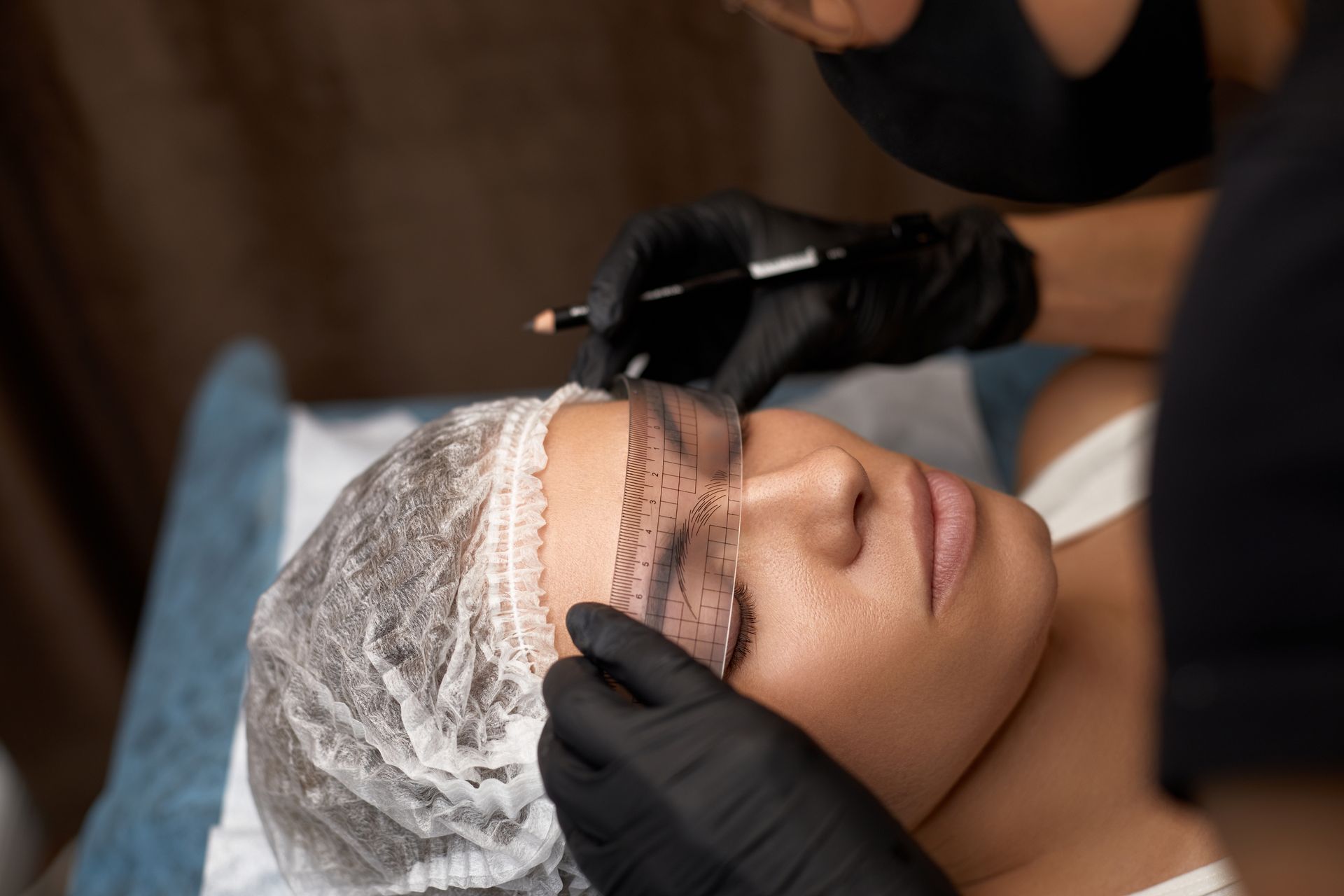 A technician applies a cosmetic treatment to a client lying back with a hair cap in a clinic setting
