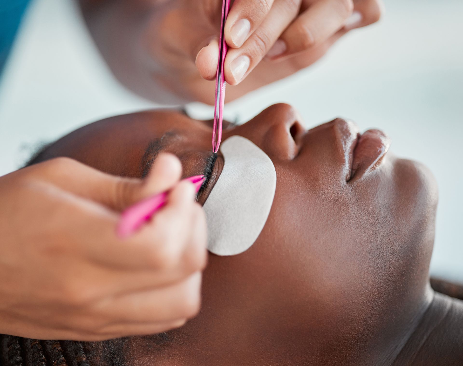Applying eyelash extensions to a reclining client with tweezers and eye pads