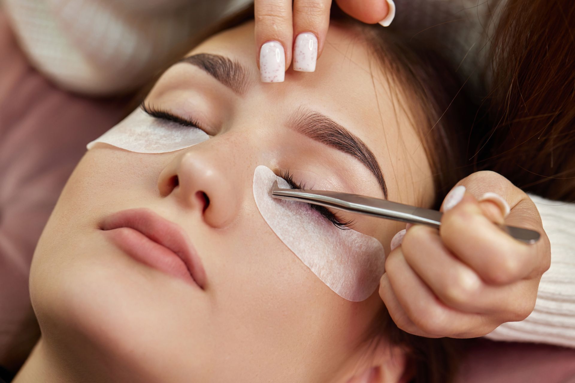 Beauty technician applying eyelash extensions to a reclining client