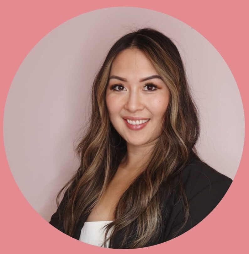 Smiling woman with long hair in black blazer against a pink circular backdrop