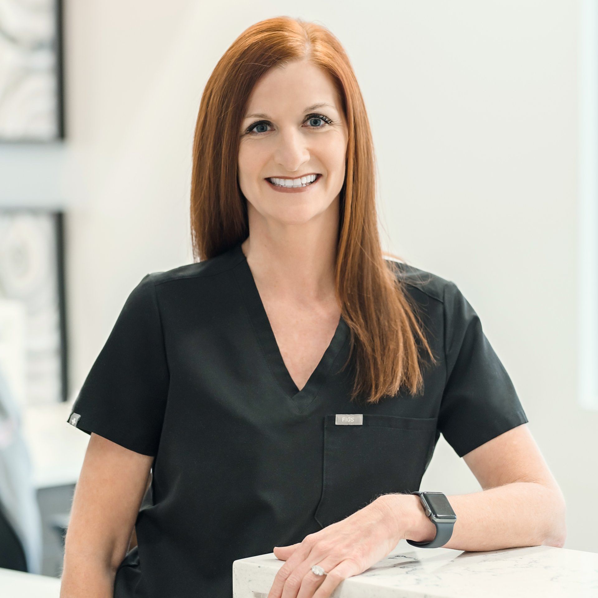 A woman in a black shirt is sitting in a chair and smiling for the camera.