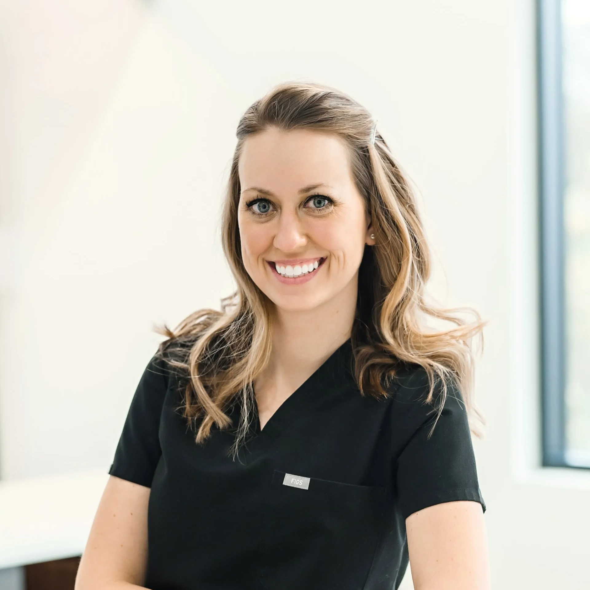 A woman in a black scrub top is smiling for the camera.