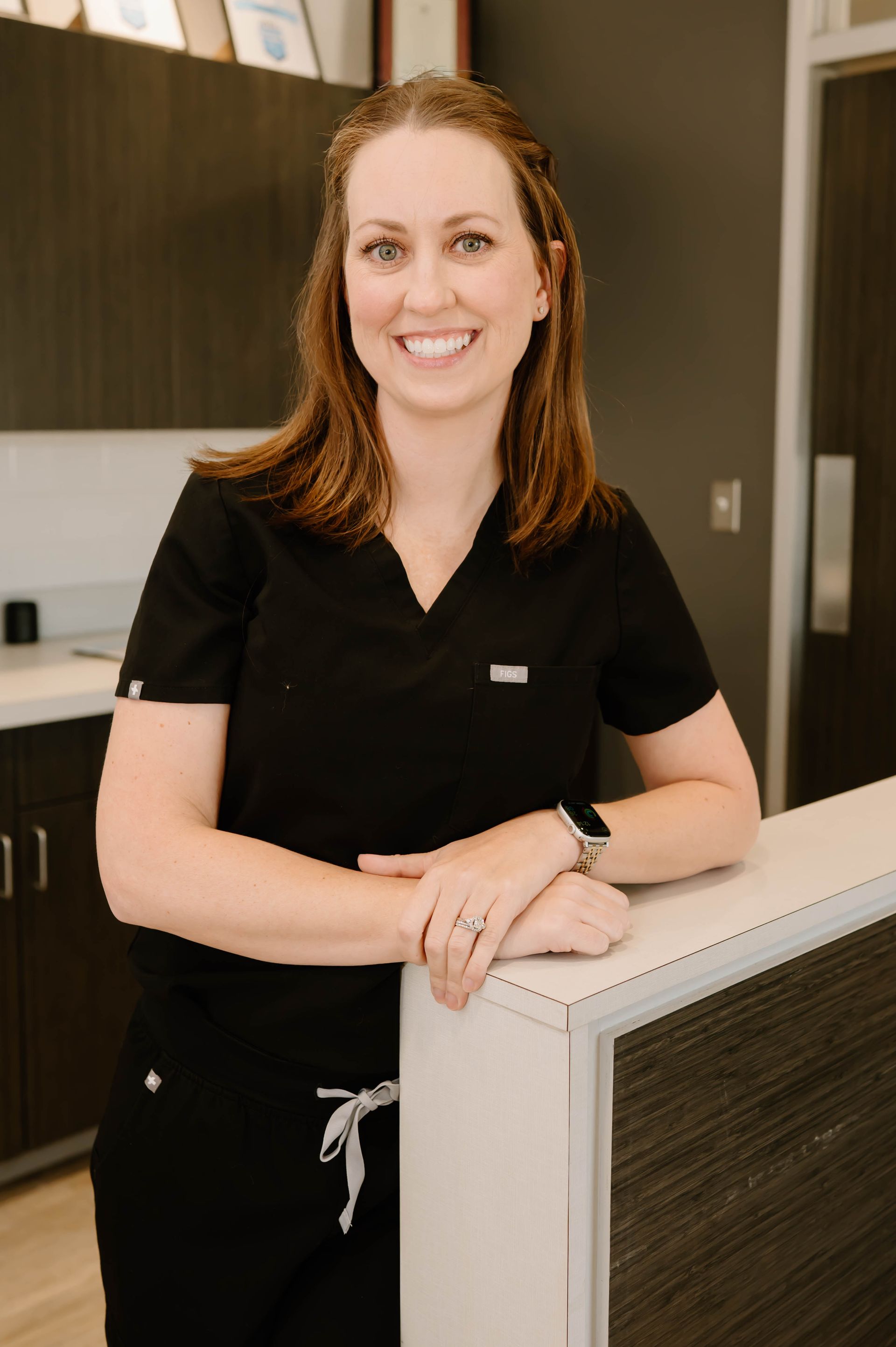A woman in a black scrub top is smiling for the camera.