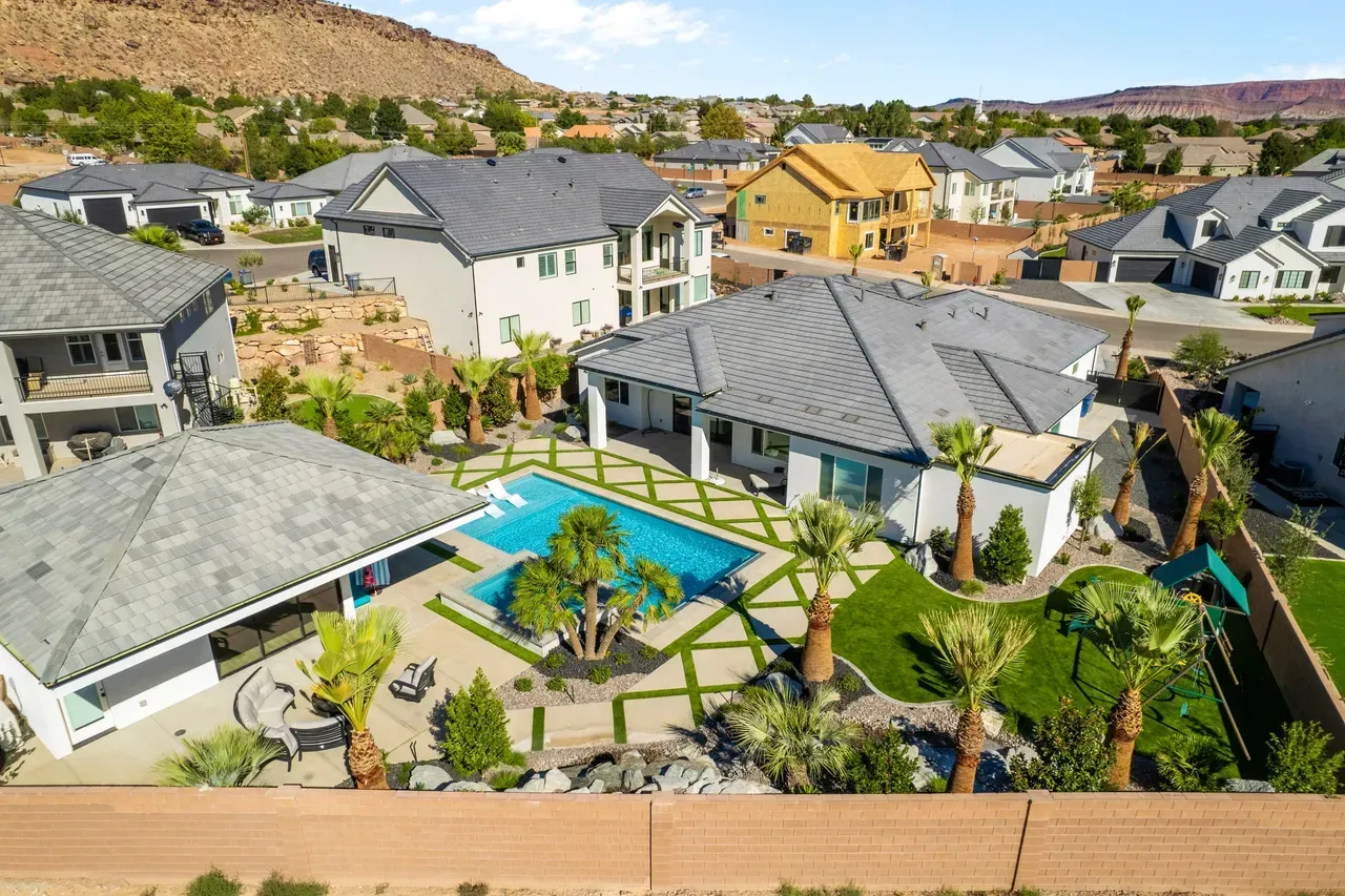 Aerial view of upscale homes with pools in a desert landscape; green lawns, blue pool, palm trees, and gray roofs.