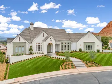 Large white house with manicured lawn, blue sky, and red rock backdrop.