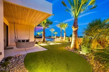 Exterior view of luxury home backyard with illuminated palm trees, swing, and green lawn at dusk.
