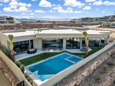 Modern house with pool, overlooking desert landscape. Blue sky, white walls, and glass windows.