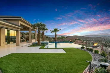 Luxury home with a pool and palm trees at dusk, overlooking a scenic valley.