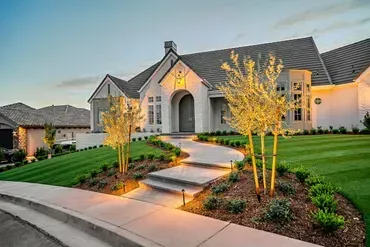 Luxury house with landscaped lawn and illuminated pathway leading to the front door at dusk.