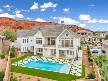 White two-story house with a pool in a yard. Red rock mountain in the background, blue sky.