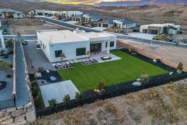 Aerial view of modern white house with green lawn in a suburban desert setting.