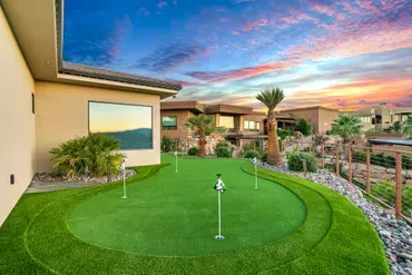 Backyard putting green with flags, next to a home with desert landscape and colorful sunset sky.