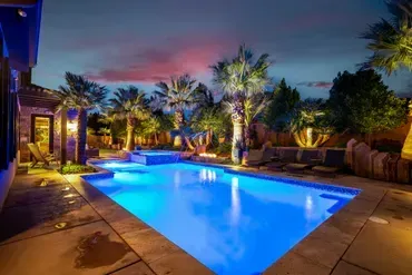 Illuminated backyard pool at twilight with palm trees and a colorful sky.