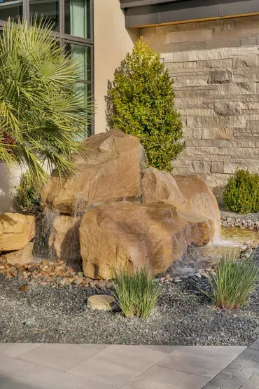 Water feature with a large rock formation and greenery, set against a stone wall.