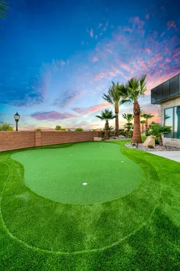 Green artificial turf putting green with palm trees against a sunset sky.