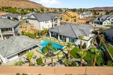 Aerial view of several modern homes with pools, lawns, and palm trees in a sunny, desert-like setting.