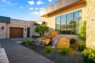 Modern home exterior with a stone facade, water feature, and garage.