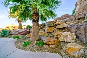 Palm tree and waterfall cascading over large rocks in a desert landscape with blue sky.