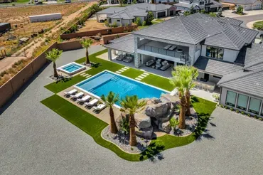 Aerial view of a luxury home with pool, spa, and artificial turf lawn surrounded by palm trees.