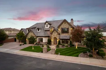Large stone-covered house with manicured lawn and a colorful sunset sky.