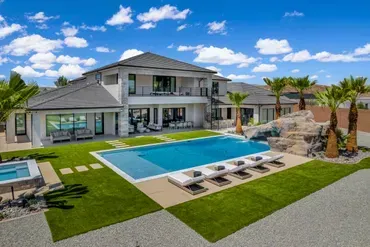 Luxury home with pool, lawn, and palm trees under a blue sky with clouds.