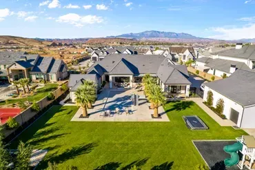 Aerial view of a large, modern home with a green lawn, patio, and mountain backdrop.