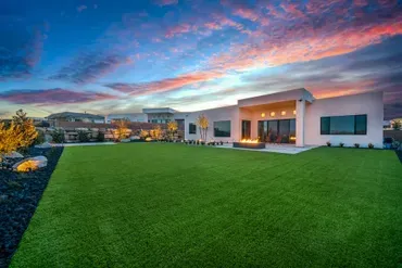 Modern home with large green lawn, fire pit, and sunset sky.
