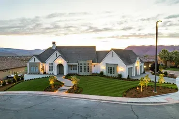 Elegant white house with gray roof, manicured lawn, and mountain backdrop at dusk.