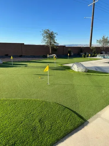 Miniature golf course with green turf, yellow flags, and rock accents against a blue sky.