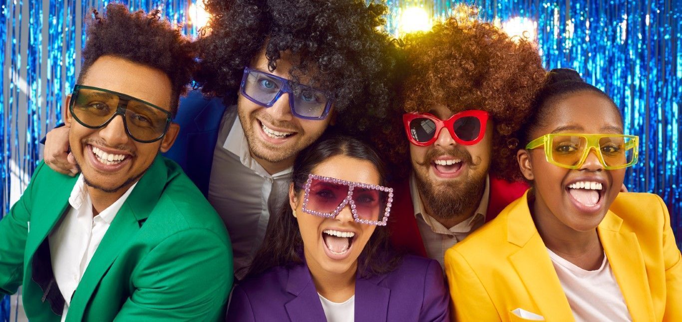 Five smiling friends wearing colorful sunglasses pose together against a sparkling blue backdrop