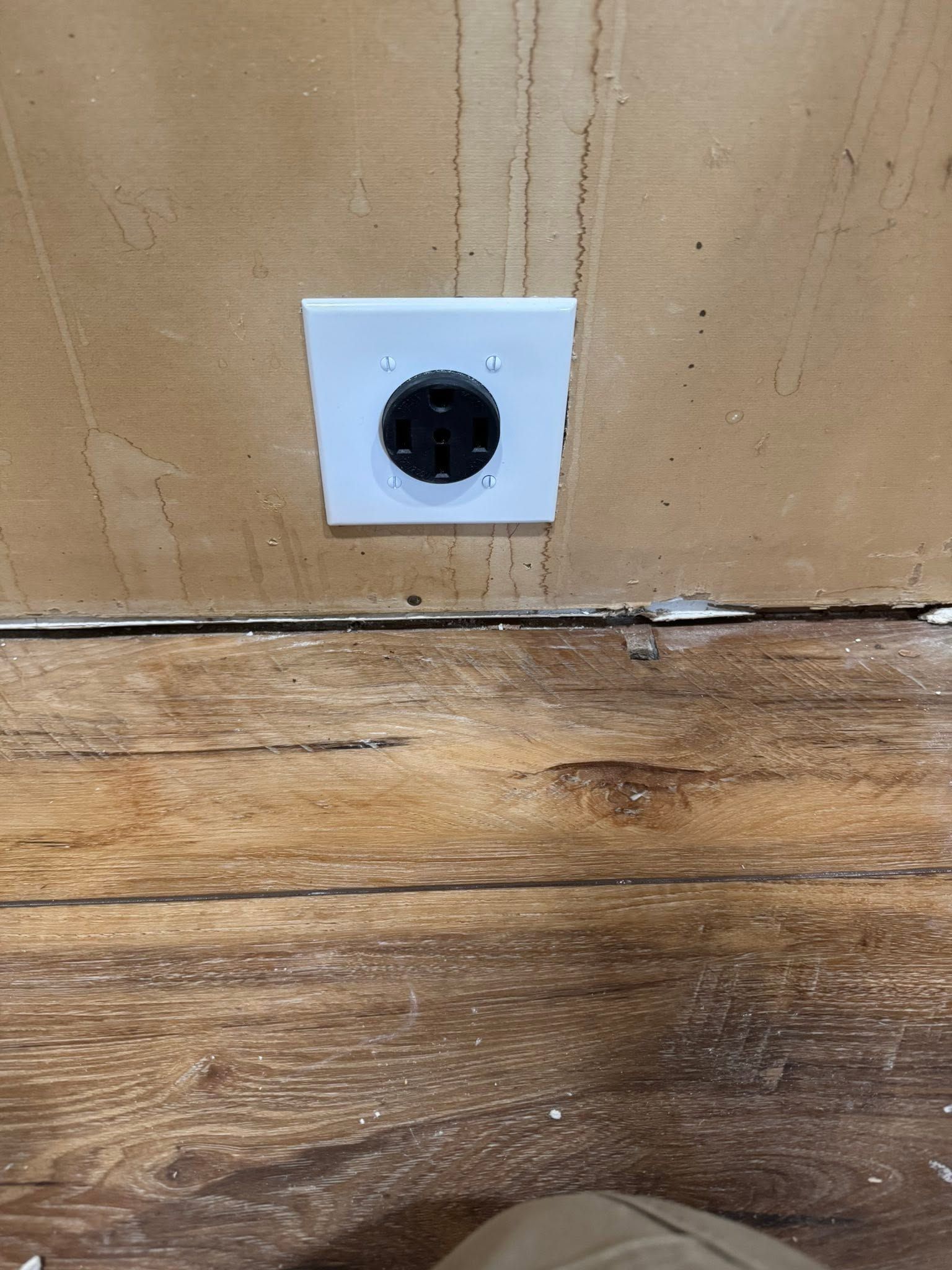 White electrical outlet on a wood-paneled wall above a worn wooden floorboard.