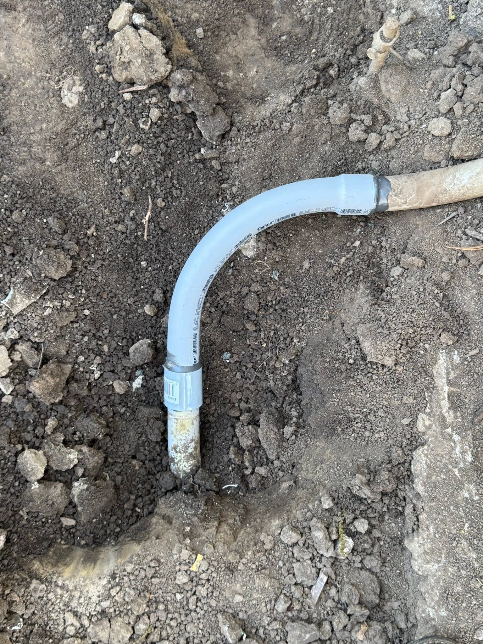 Light blue plastic pipe elbow in dirt beside a beige hose connector