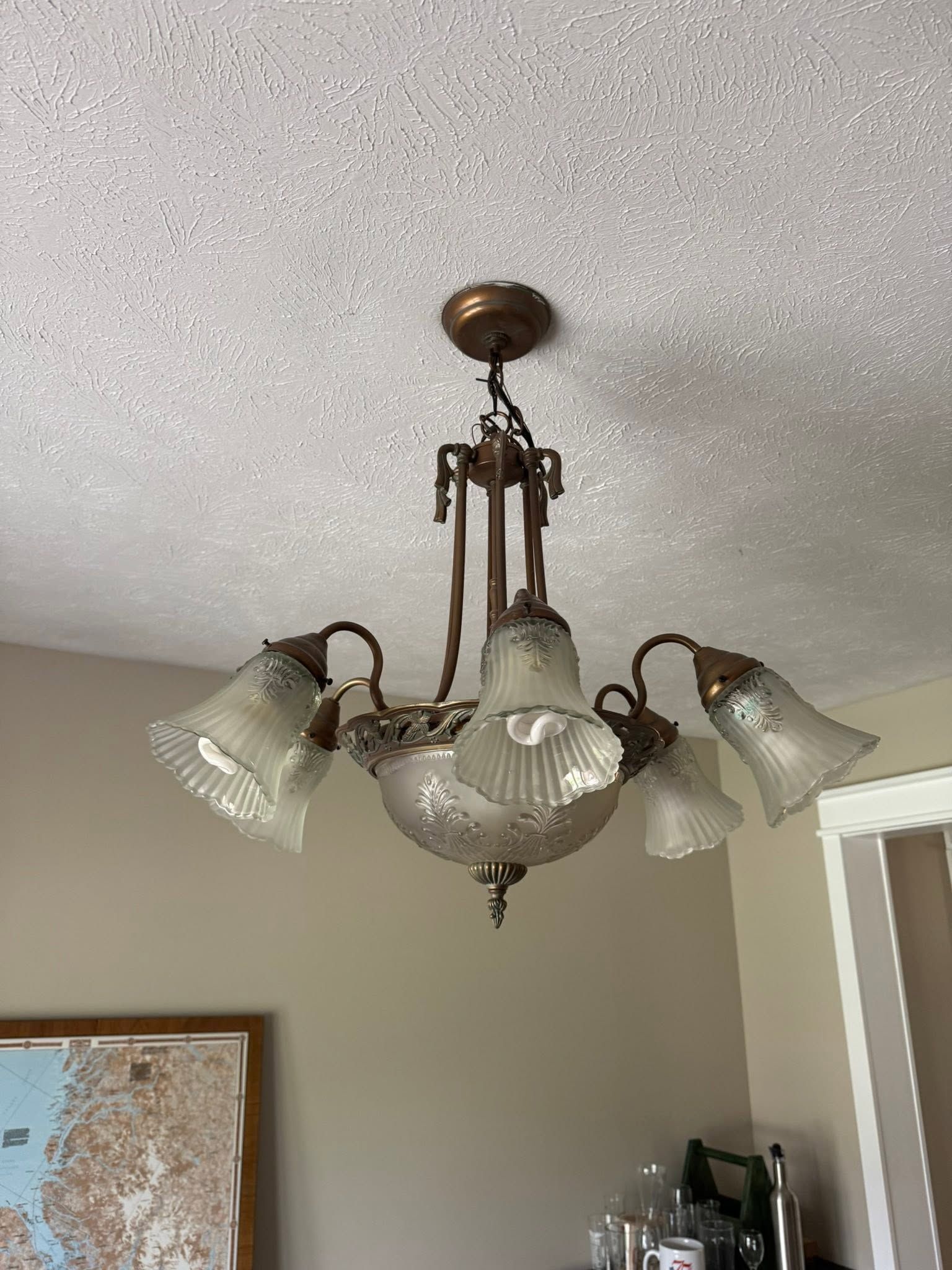 Brass chandelier with frosted glass shades hanging from a textured white ceiling in a room.