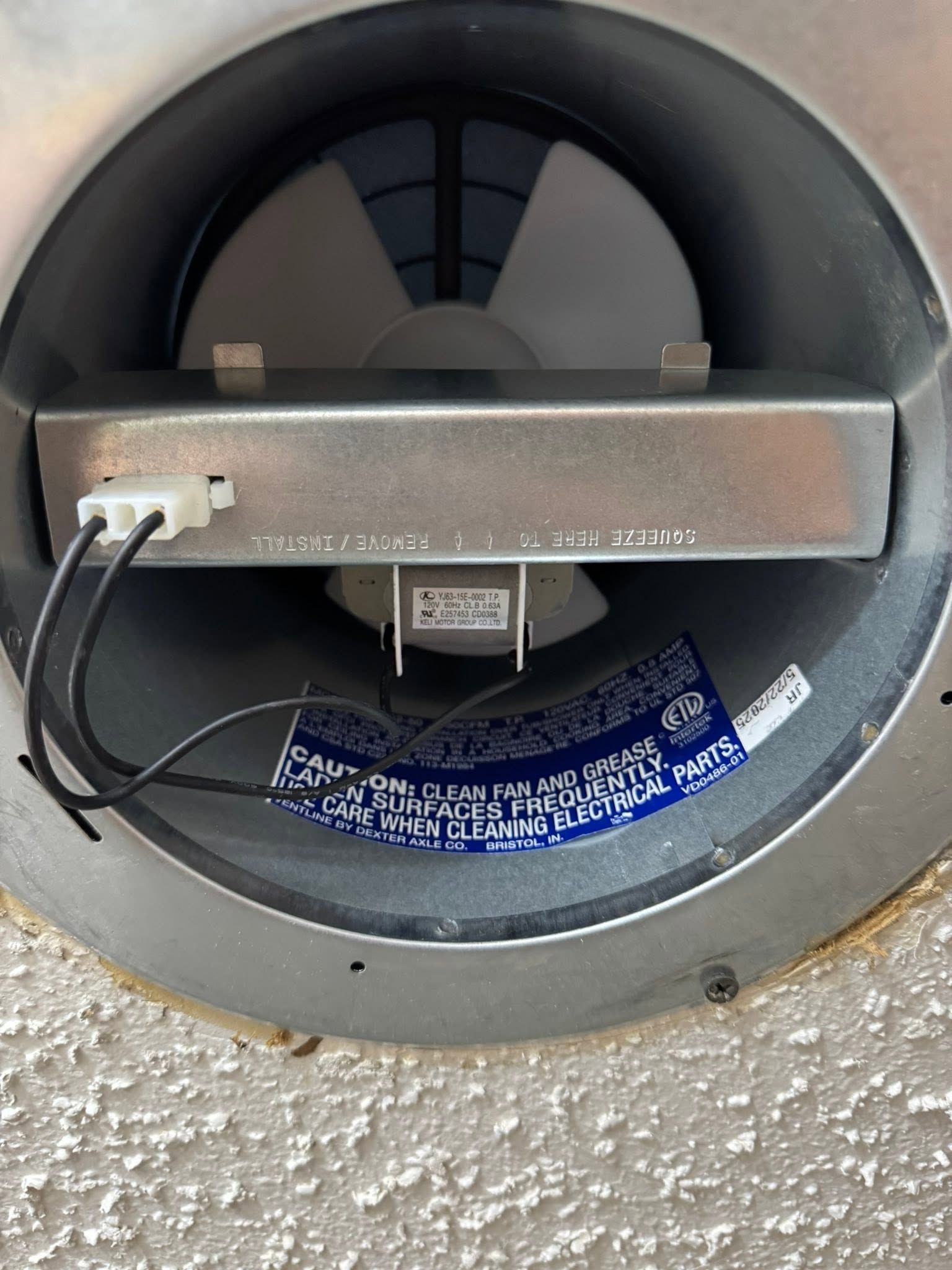 Close-up of a round gray device with wiring and a blue label mounted on a textured wall.