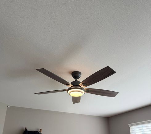 Dark ceiling fan with light on a white ceiling in a gray room