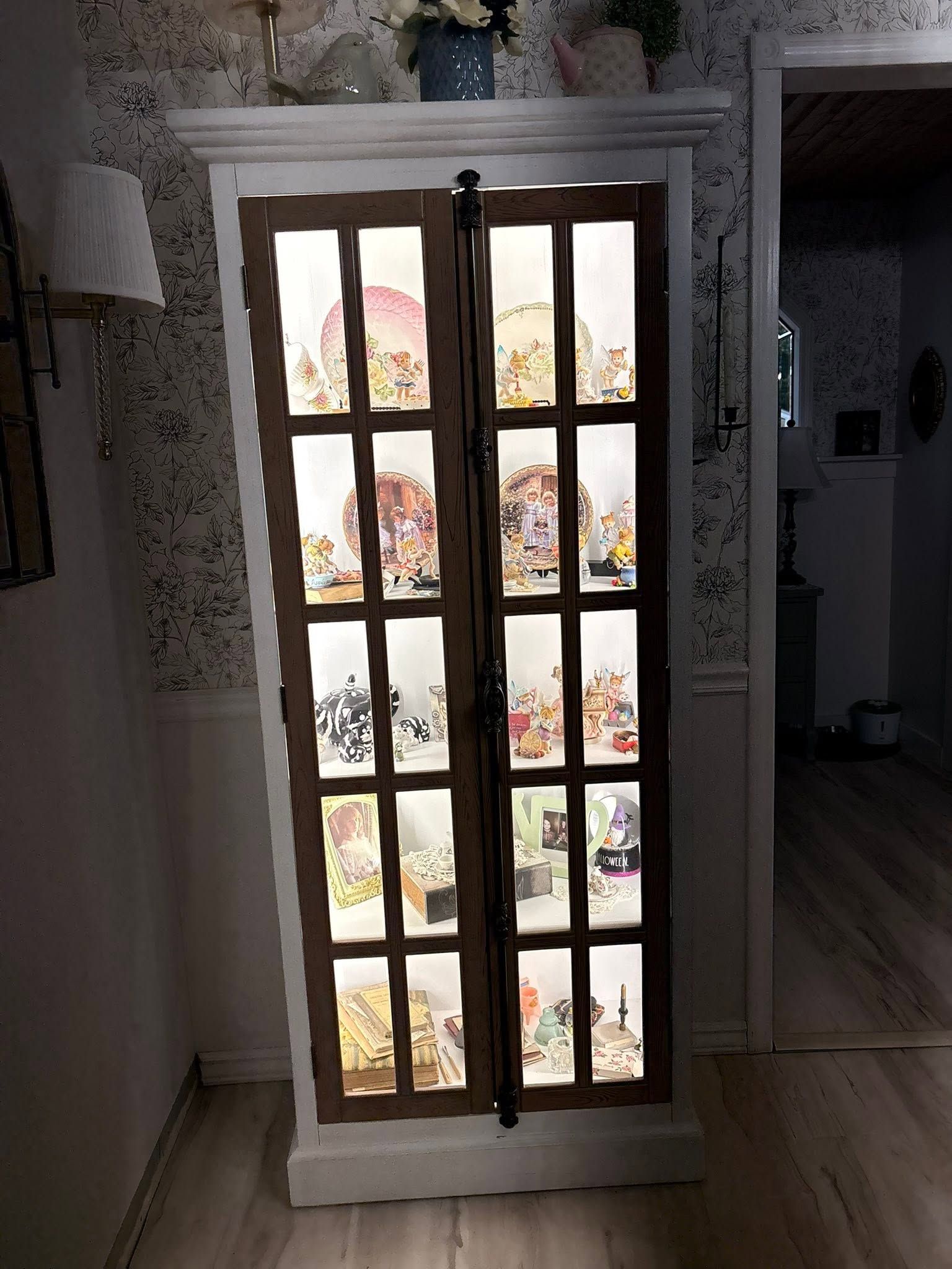 White cabinet with glass panes displaying colorful items inside, in a dim room.