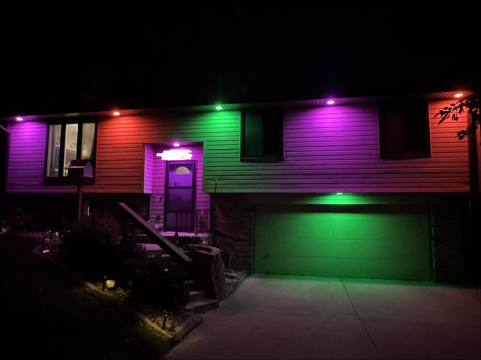 House exterior at night with purple and green accent lights illuminating the front and garage.