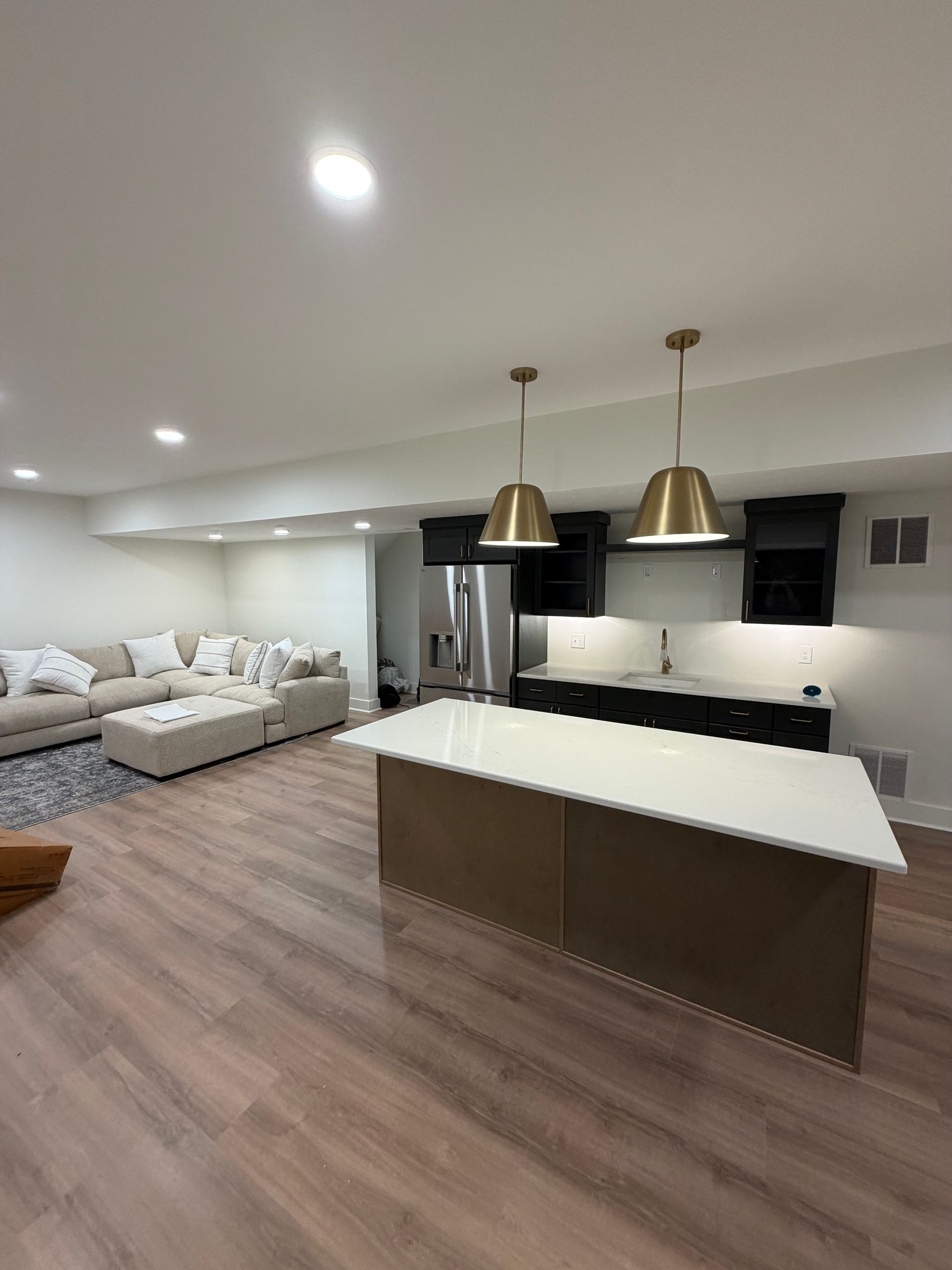 Modern open-plan living room and kitchen with white sofas, island countertop, and pendant lights