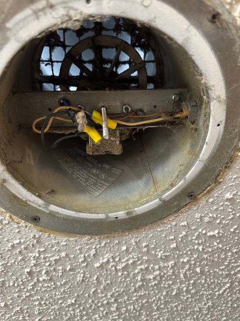 Damaged circular wall vent with exposed wires, yellow tape, and dust buildup
