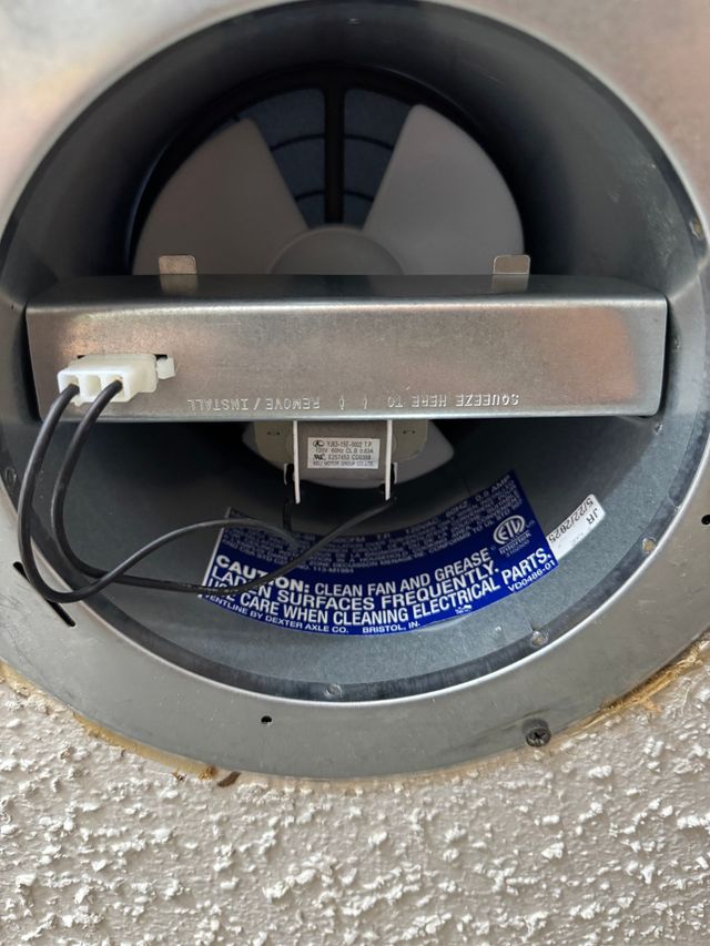 Round recessed wall speaker with a metal bar and wires visible against a textured wall.