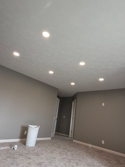 Empty carpeted room with beige walls, recessed ceiling lights, and a doorway in the back corner