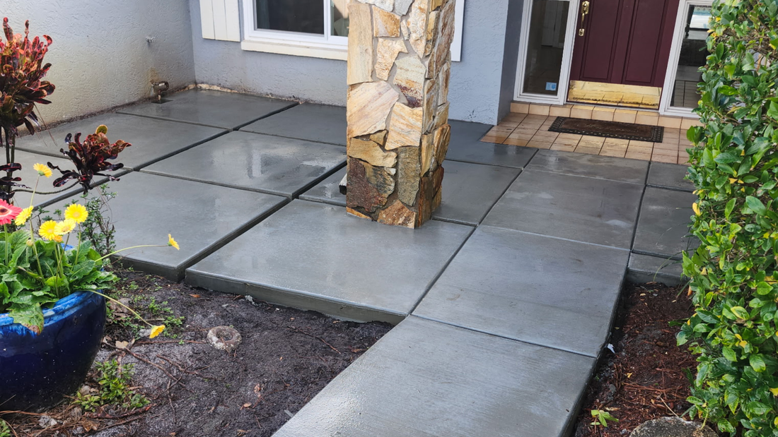 Exterior with concrete pavers leading to a door, a stone column in the center. 