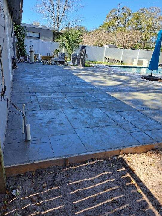 Concrete patio next to a house and pool, with wooden border and pipes.