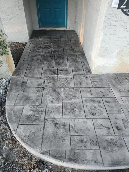 Grey stone-patterned concrete walkway leading to a turquoise door of a home.