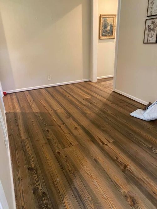 Empty hallway with wood-look flooring and beige walls, featuring framed art and a white bag on the floor