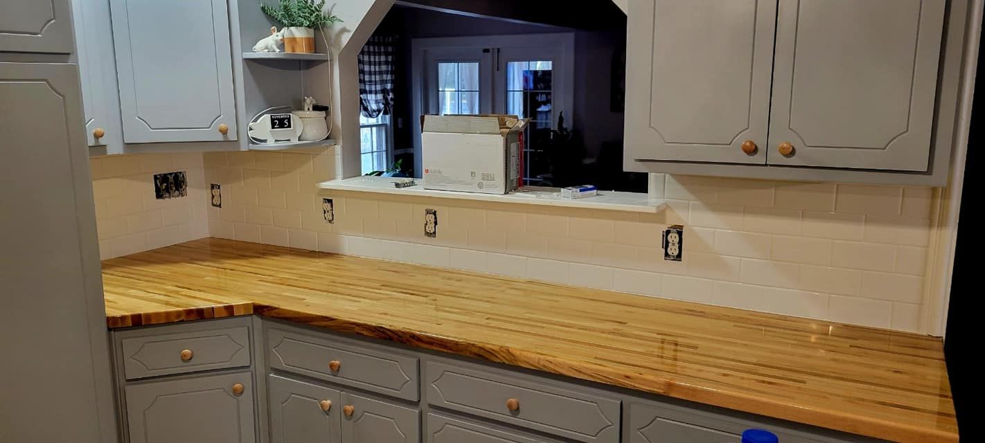 Kitchen countertop with light wood butcher block, white cabinets, and a window over the sink