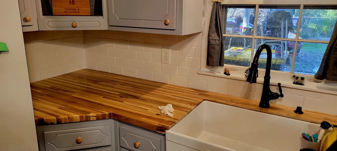 Kitchen corner with butcher-block countertop, white cabinets, sink, and window above a black faucet